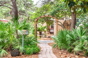 Un sentier de jardin mène à une arche en bois, entourée d’une végétation luxuriante et d’une clôture rustique.