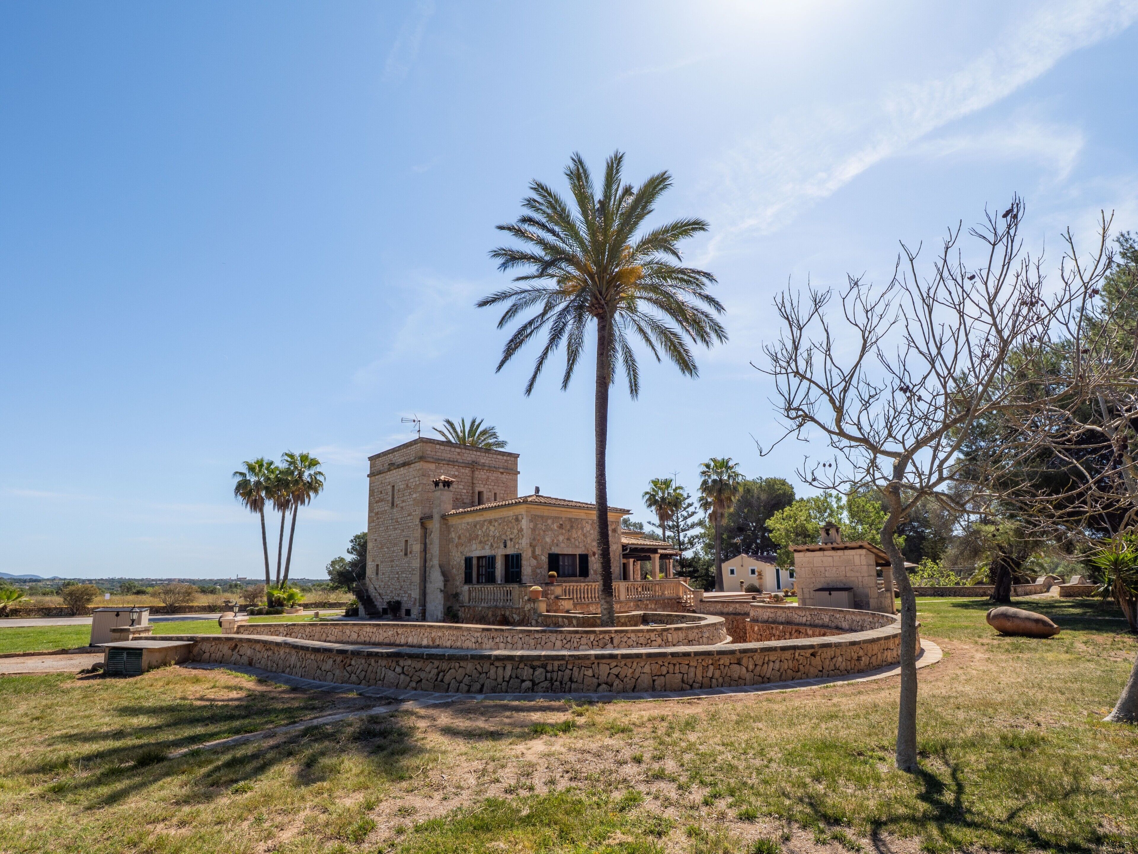 A stone building with a circular courtyard, palm trees, and a clear sky.