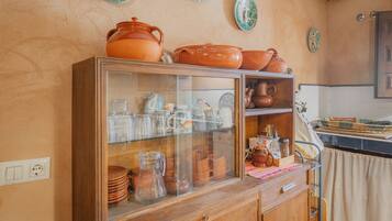Una cocina con un armario de madera que contiene varios utensilios de cocina, una vitrina de vidrio y platos decorativos en la pared.
