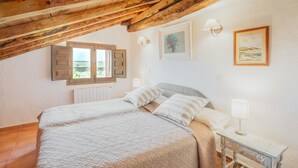 Et soveværelse med seng, et natbord, en lampe, et vindue med skodder og et billede på væggen.