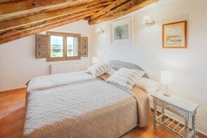 A bedroom with a wooden ceiling, a bed with a quilt, a nightstand, and a window with shutters.