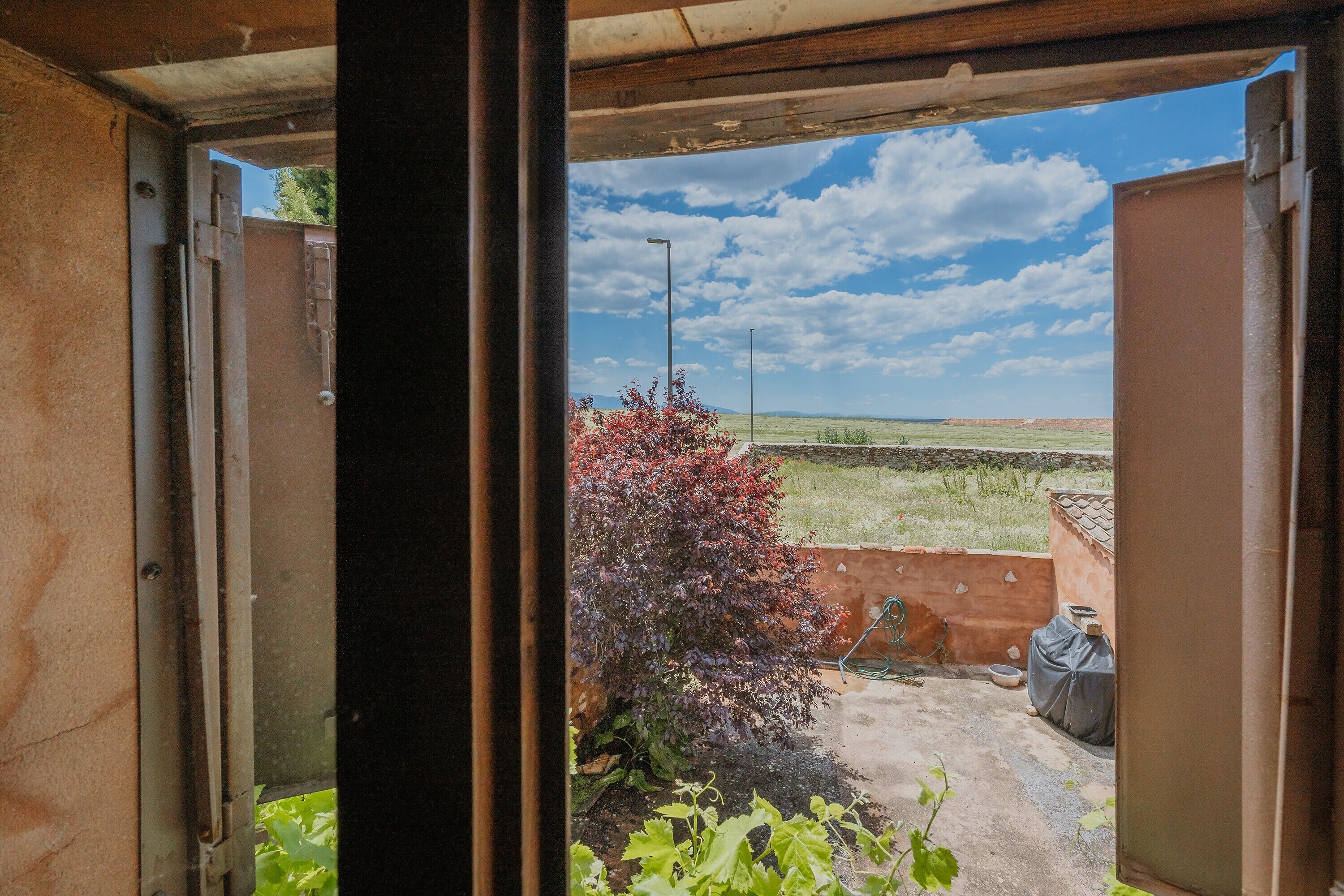 Une porte ouverte donnant sur un jardin, avec un ciel dégagé et un buisson.
