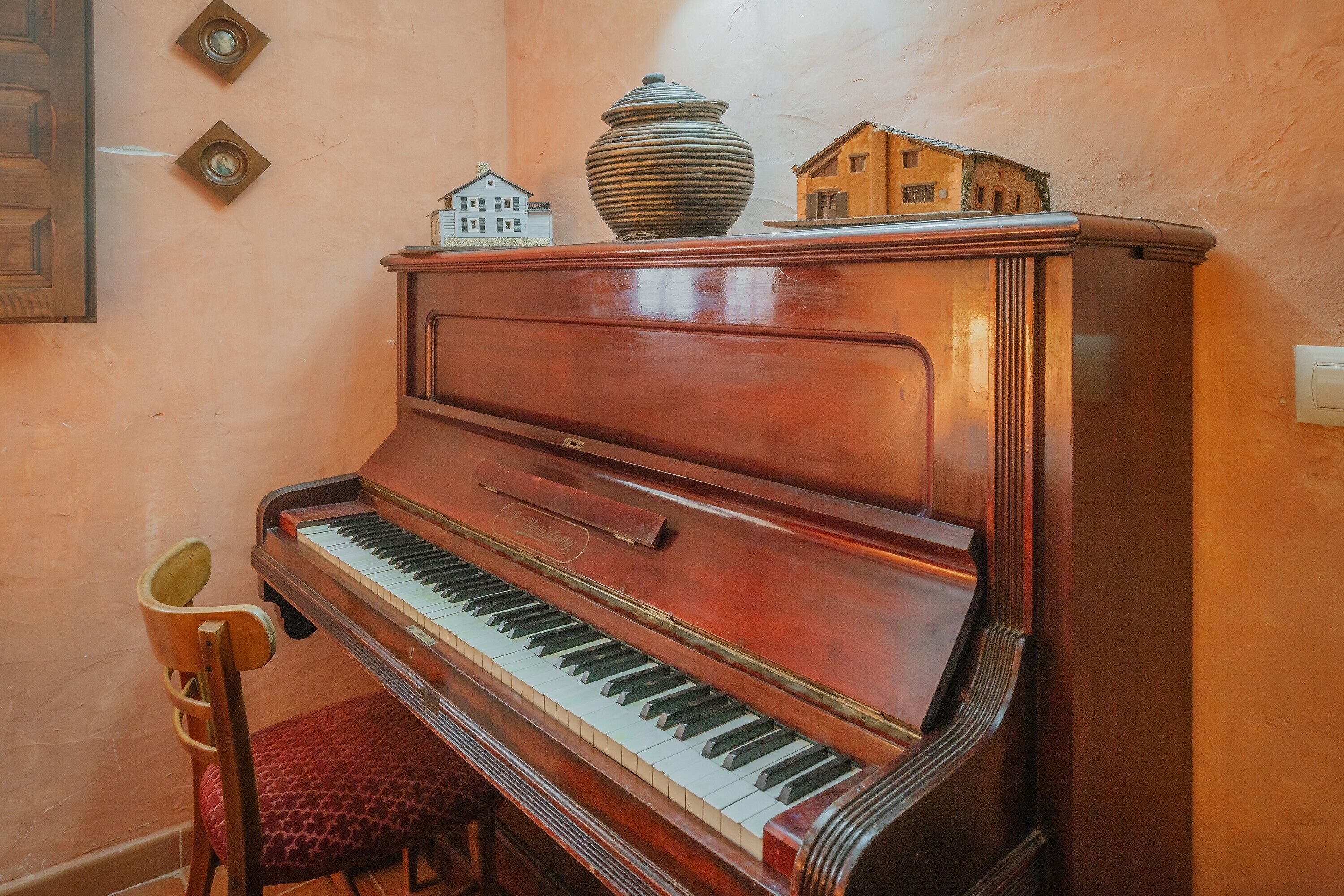 Un piano à queue avec un placage en bois, un fauteuil rouge rembourré et de petites maisons miniatures posées sur le dessus.
