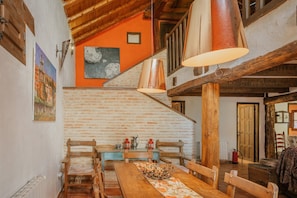 Un interior rústico con una mesa de comedor de madera, bancos, una escalera y lámparas colgantes.