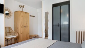 A bedroom with a bed, wooden wardrobe, wicker chair, and a unique wall design.