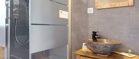 A bathroom with a glass-enclosed shower, a wooden vanity with a large stone basin, and a mirror on the wall.