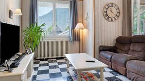 Een kamer met een geruite vloer, een bruine leren bank, een witte tafel, een televisie, een lamp en een wandklok.