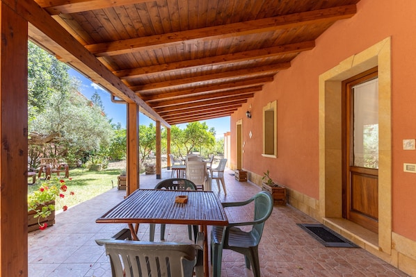 Un patio al aire libre con techo de madera, una mesa, sillas y plantas en macetas.