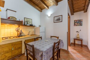 A kitchen with wooden cabinets, a tiled backsplash, a dining table with chairs, a refrigerator, and a wall-mounted light.