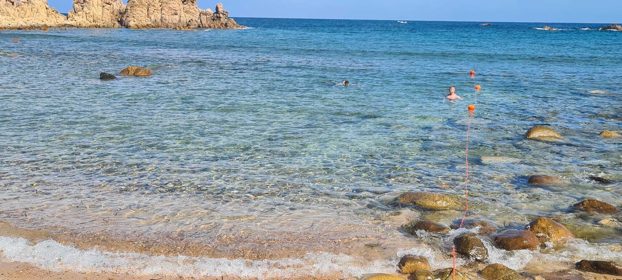 Una playa con agua cristalina, rocas y una costa rocosa distante.