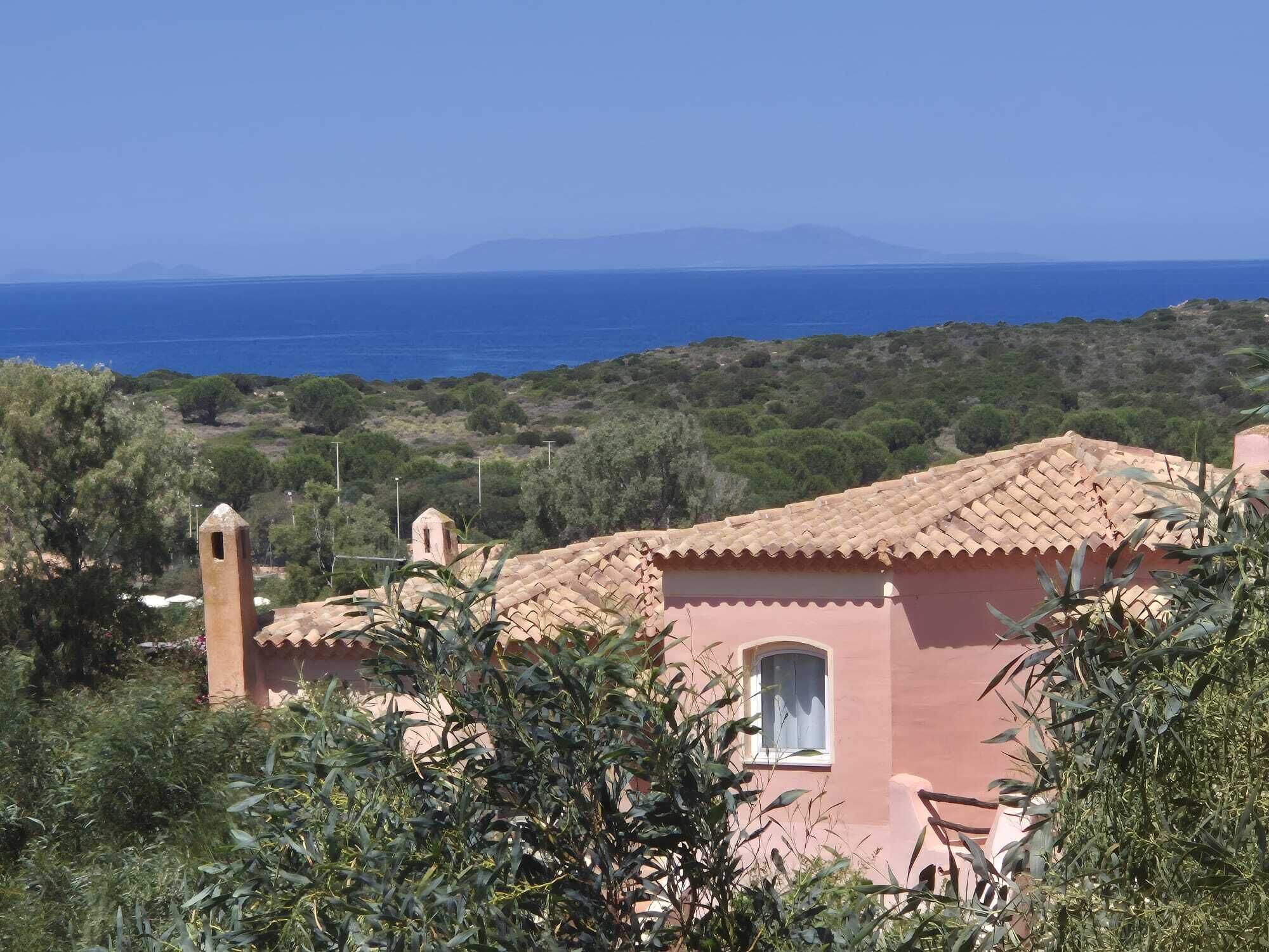 A Mediterranean-style building with a terracotta roof, surrounded by greenery and overlooking a coastal landscape.