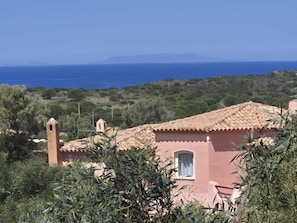 Ein Gebäude im mediterranen Stil mit Terrakotta-Dachziegeln, umgeben von Grün und mit Blick auf eine Küstenlandschaft.