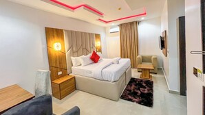A modern hotel room with a bed, bedside tables, a sofa, a TV, and a ceiling with red lighting.
