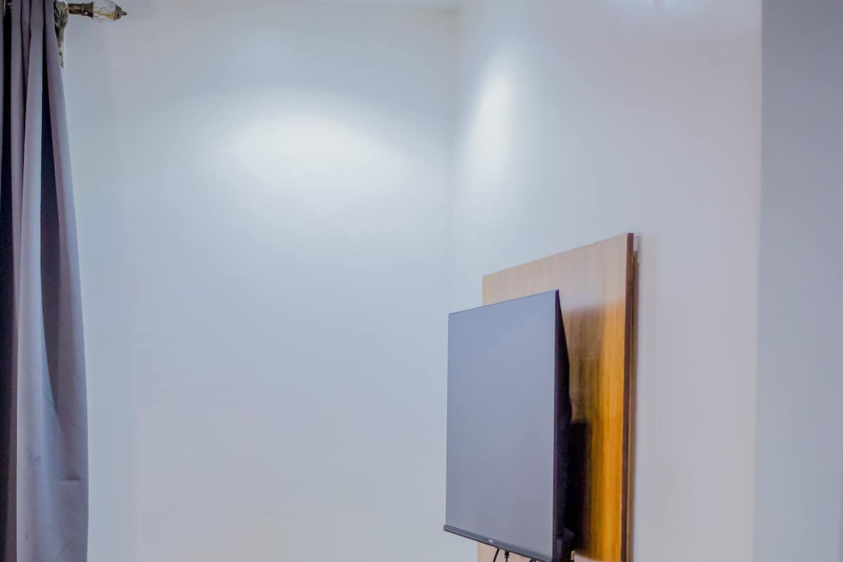 Ein Zimmer mit einer Couch, einem Holztisch, einem an der Wand montierten Fernseher und einem Vorhang.