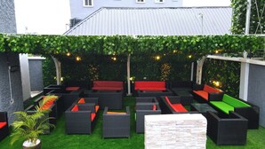 An outdoor seating area with multiple black wicker sofas and chairs, some with red cushions, arranged on artificial grass.
