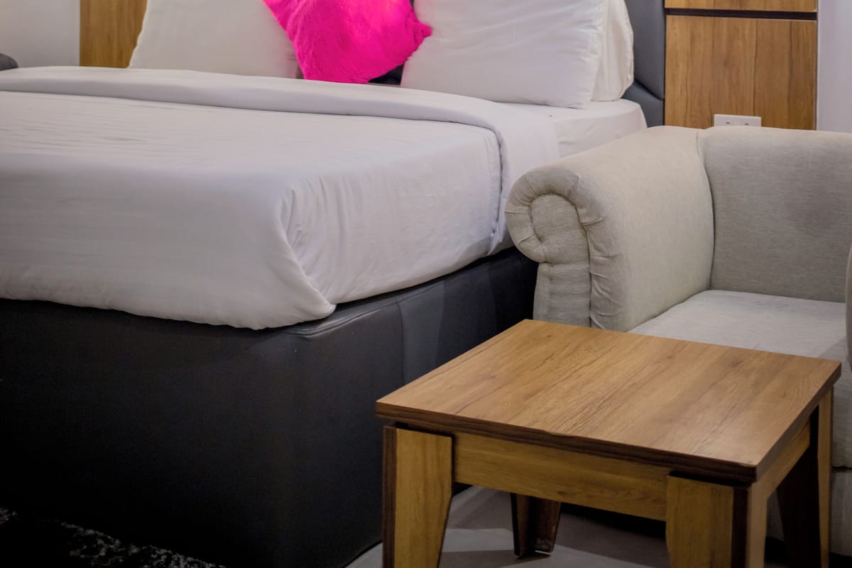 Ein modernes Hotelzimmer mit einem Bett, einer Couch, einem Holznachttisch und einem Kopfteil mit integrierter Beleuchtung.