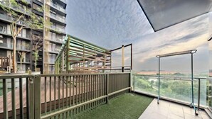 Un balcón con vista a un paisaje urbano, un área de césped artificial verde y una barandilla metálica.