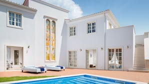 Ein weißes Gebäude mit Swimmingpool, großen Fenstern und einer überdachten Terrasse.