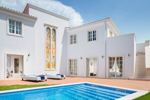 Um edifício branco com piscina, amplas janelas e um espaço de estar coberto.