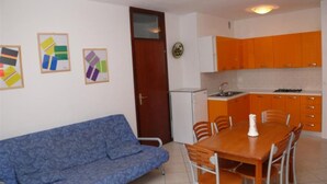 A compact living space with a sofa, dining table, chairs, a kitchenette, and wall art. - Welcoming Apartment for Seven Guests in Bibione (San Michele al Tagliamento)