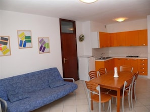 Un espace de vie compact comprenant un canapé, une table à manger, des chaises, un coin cuisine et des œuvres d’art murales.