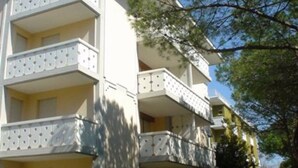 A multi-story building with balconies, a flat roof, and a clear sky. - Welcoming Apartment for Seven Guests in Bibione (San Michele al Tagliamento)