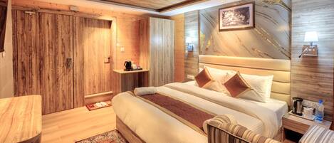 A hotel room with a wooden ceiling, a bed with multiple pillows, a bedside table with a lamp, and a small shelf with a coffee maker.