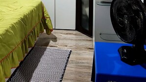 Ein Schlafzimmer mit Bett, Ventilator, Schreibtisch, Kleiderschrank und Ablage für Toilettenartikel.