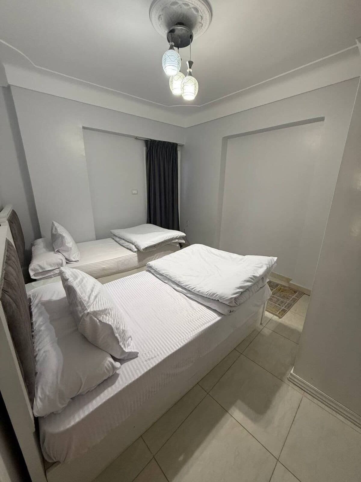 Een slaapkamer met twee bedden, een plafondlamp en een raam met gordijnen.