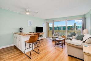 A spacious living area with a kitchen, dining area, and a balcony with a view. - Coastal Condo Steps to Beach & Attractions (Daytona Beach)