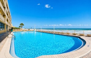 A clear blue pool with a wooden deck, a palm tree, and a view of the ocean. - Coastal Condo Steps to Beach & Attractions (Daytona Beach)