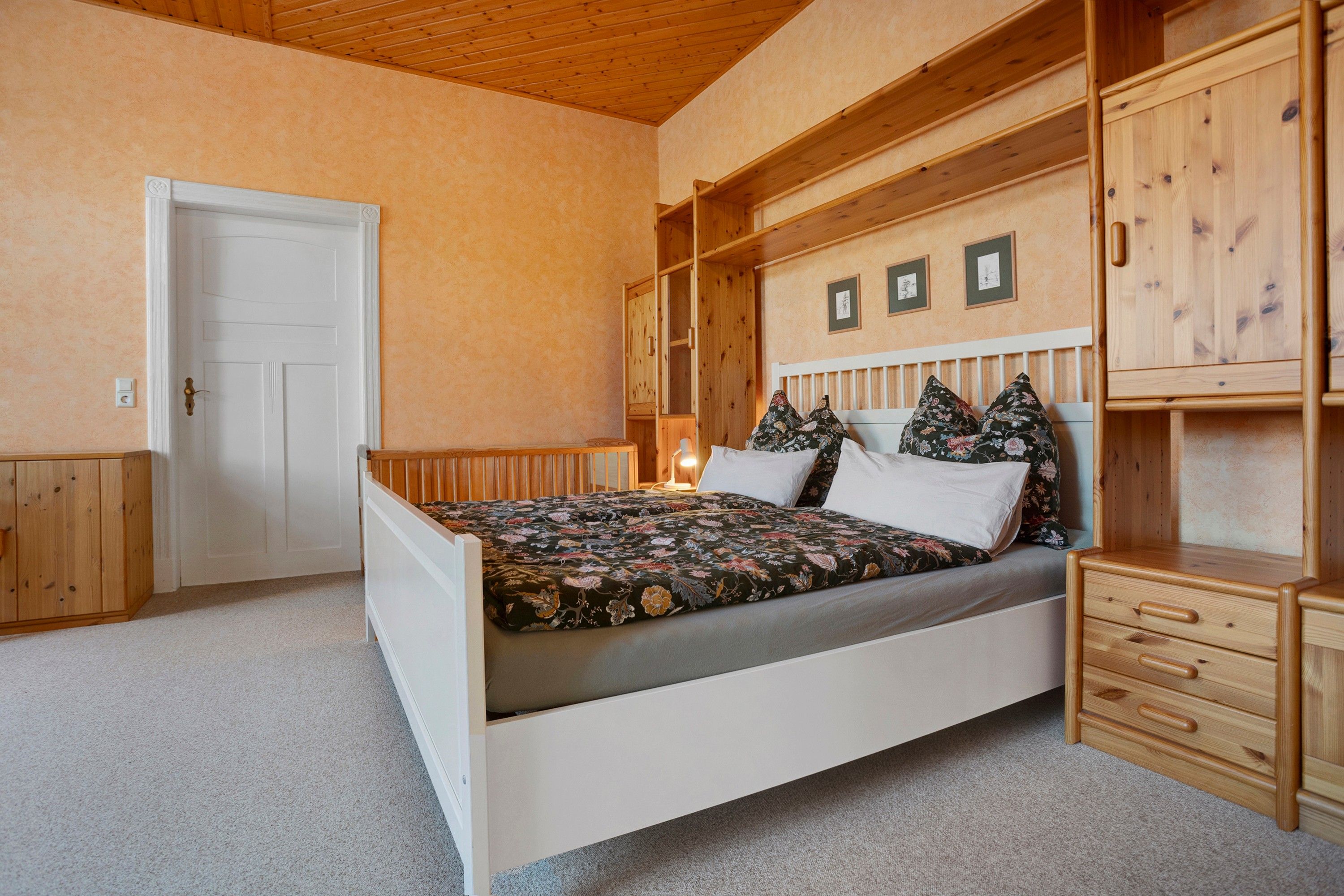 A bedroom with a bed, wooden headboard, a nightstand, a dresser, and a door.