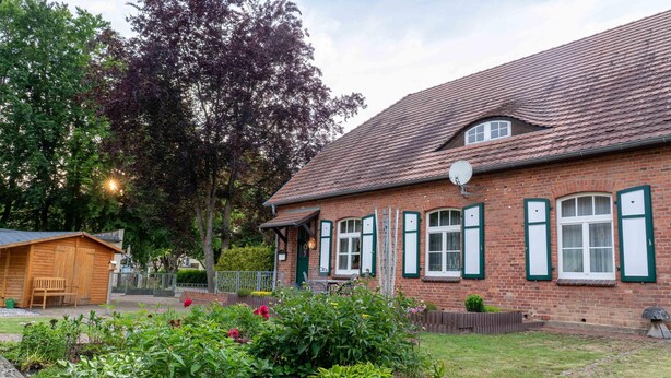 A brick building with a sloped roof, a small wooden shed, and a garden with various plants. - Holiday Home 'Ivenack Old School' with Private Terrace and Private Garden (Ivenack)