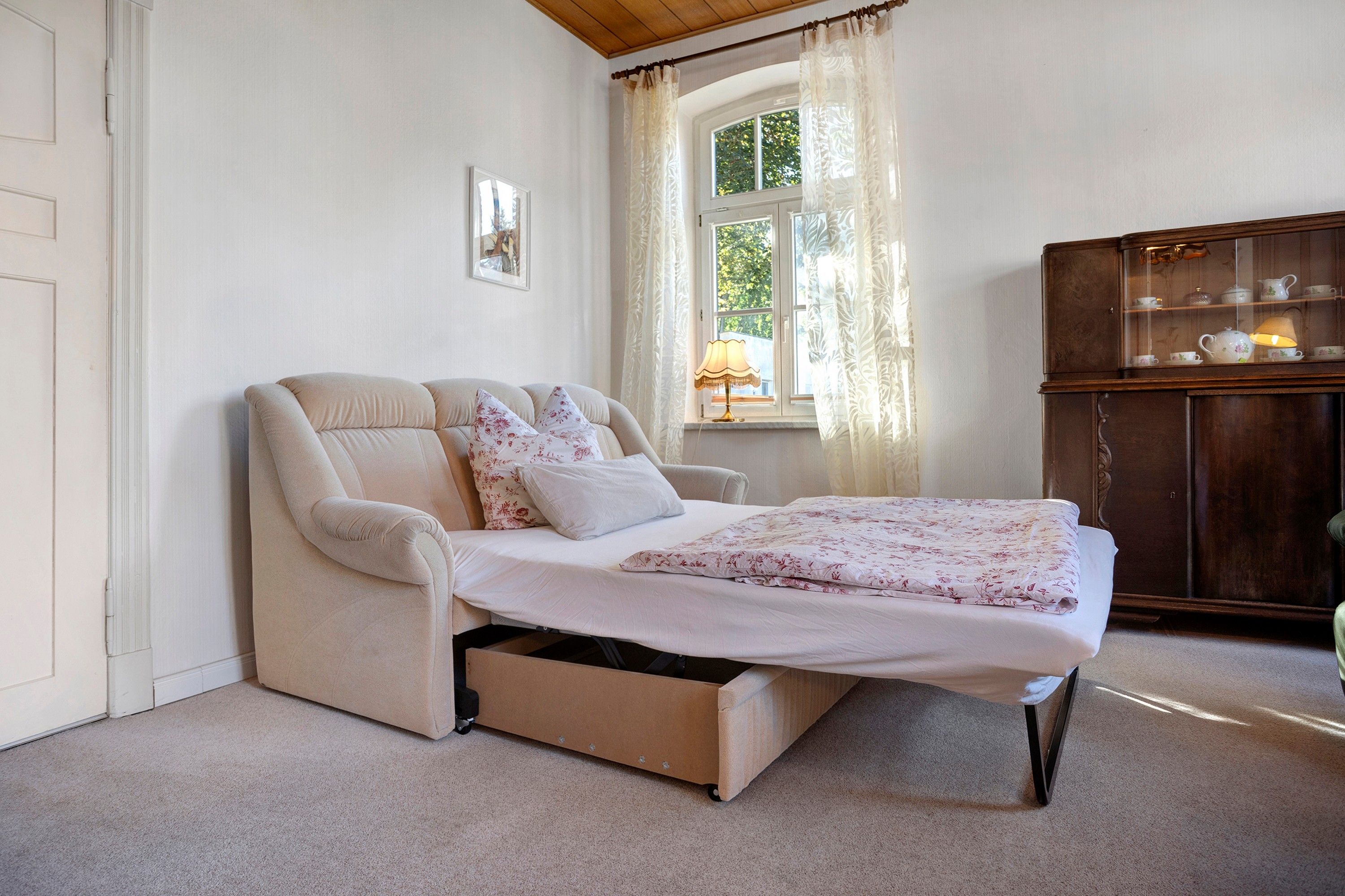 A bedroom with a bed, a chair, a cabinet, and a window with curtains.