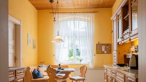 A kitchen with wooden cabinets, a dining table, chairs, a window with curtains, and a hanging light fixture. - Holiday Home 'Ivenack Old School' with Private Terrace and Private Garden (Ivenack)