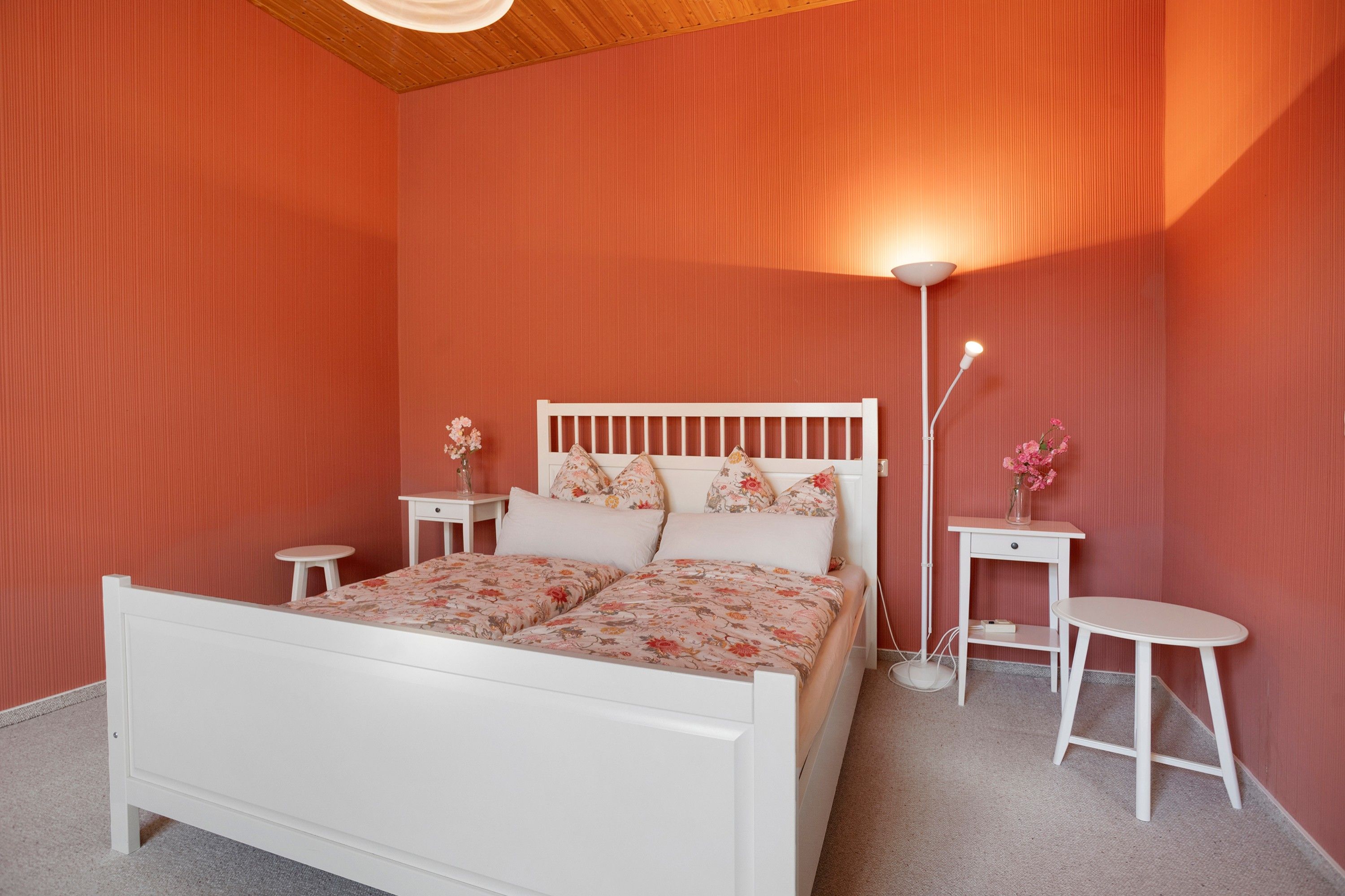 A bedroom with a white bed, floral bedding, a nightstand, a bedside table, and a floor lamp.