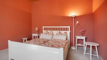 A bedroom with a white bed, floral bedding, a nightstand, a bedside table, and a floor lamp.