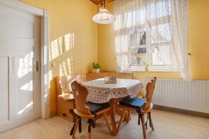 A dining area with a table and chairs, a window with lace curtains, and a radiator. - Holiday Home 'Ivenack Old School' with Private Terrace and Private Garden (Ivenack)