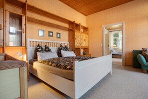 A bedroom with a bed, wooden headboard, built-in shelves, and a window with curtains.