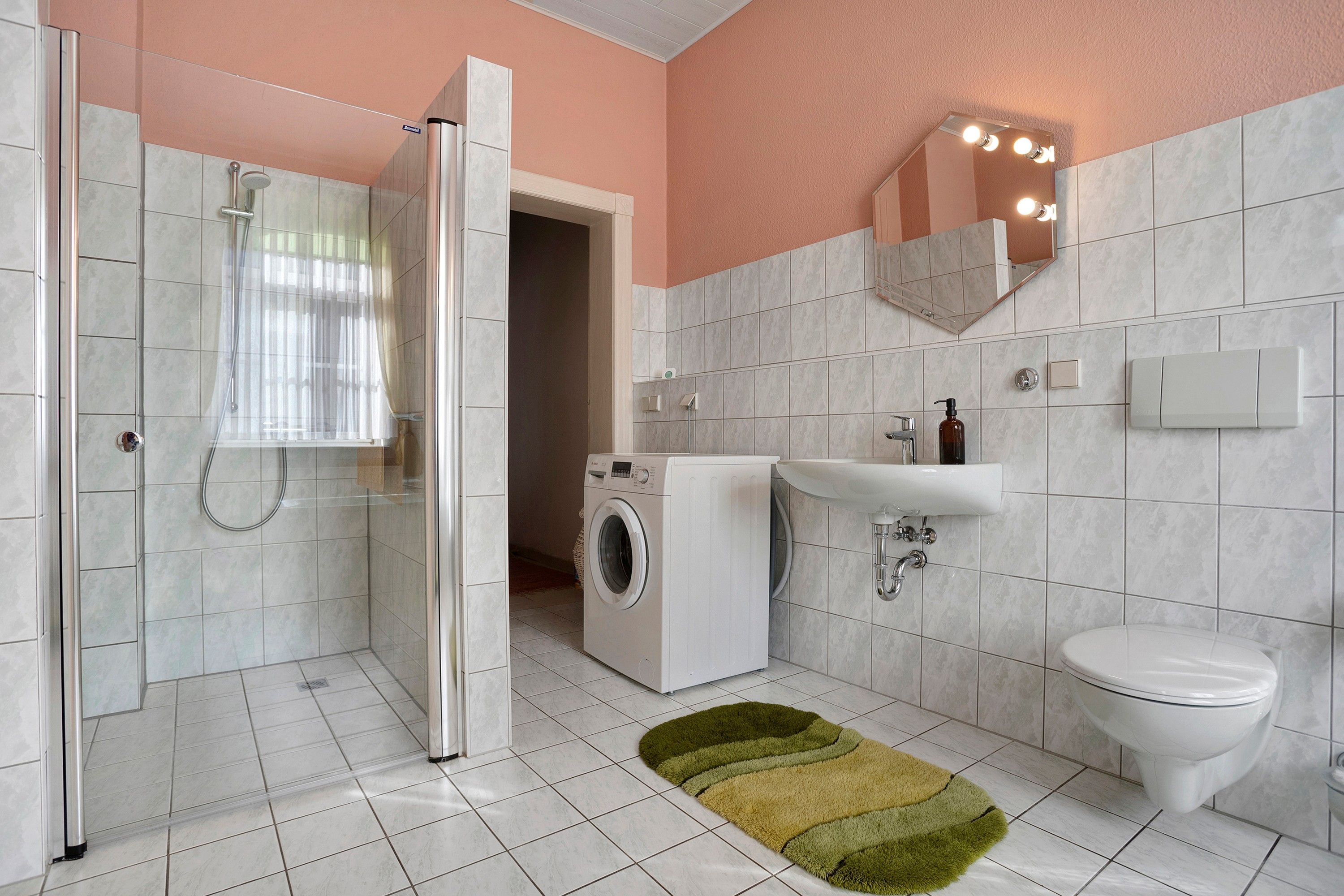 Une salle de bain équipée d’une douche, d’un lave-linge, d’un lavabo et de toilettes.