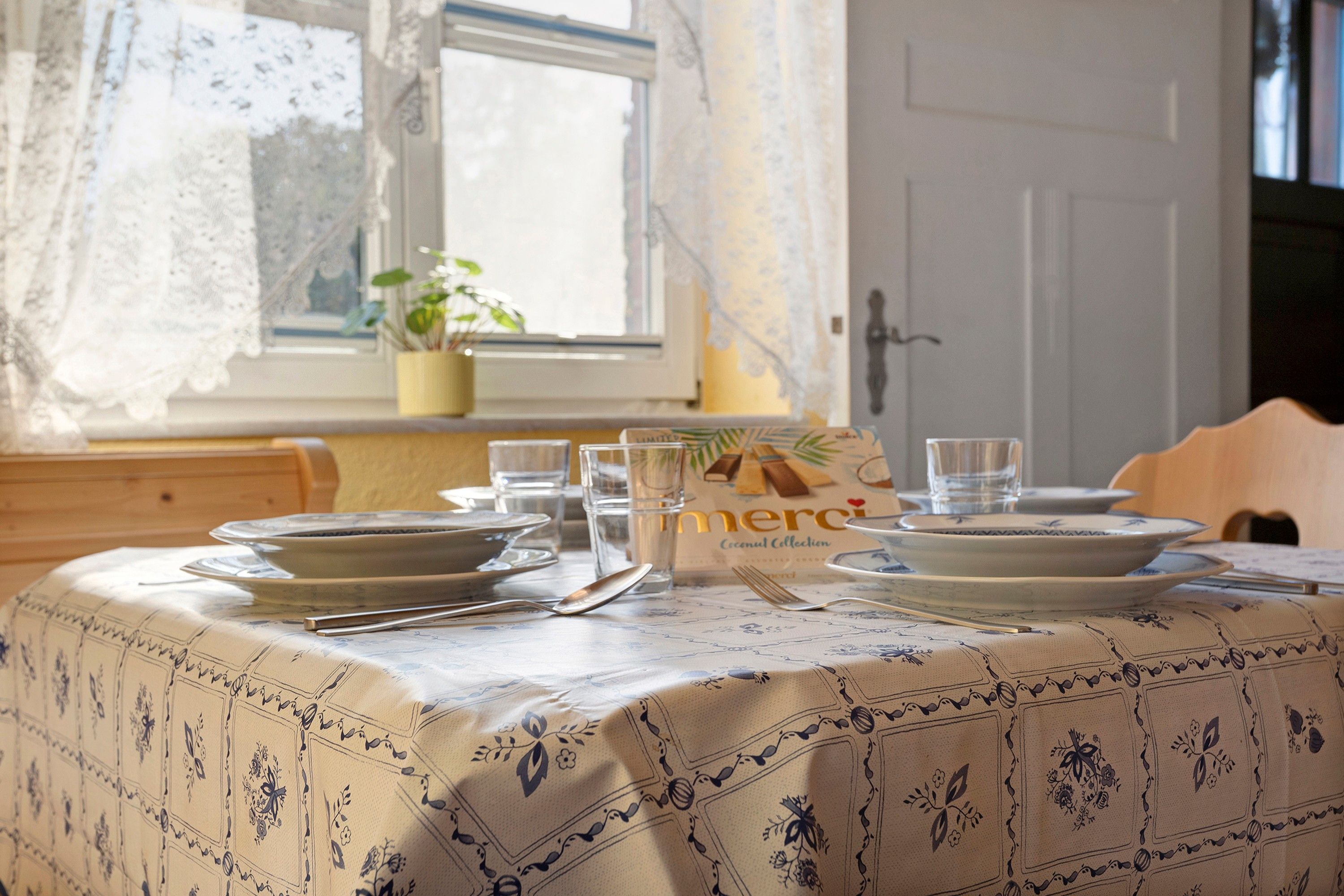 A dining table set with plates, cutlery, and glasses, with a 'merci' sign indicating a thank you gesture.