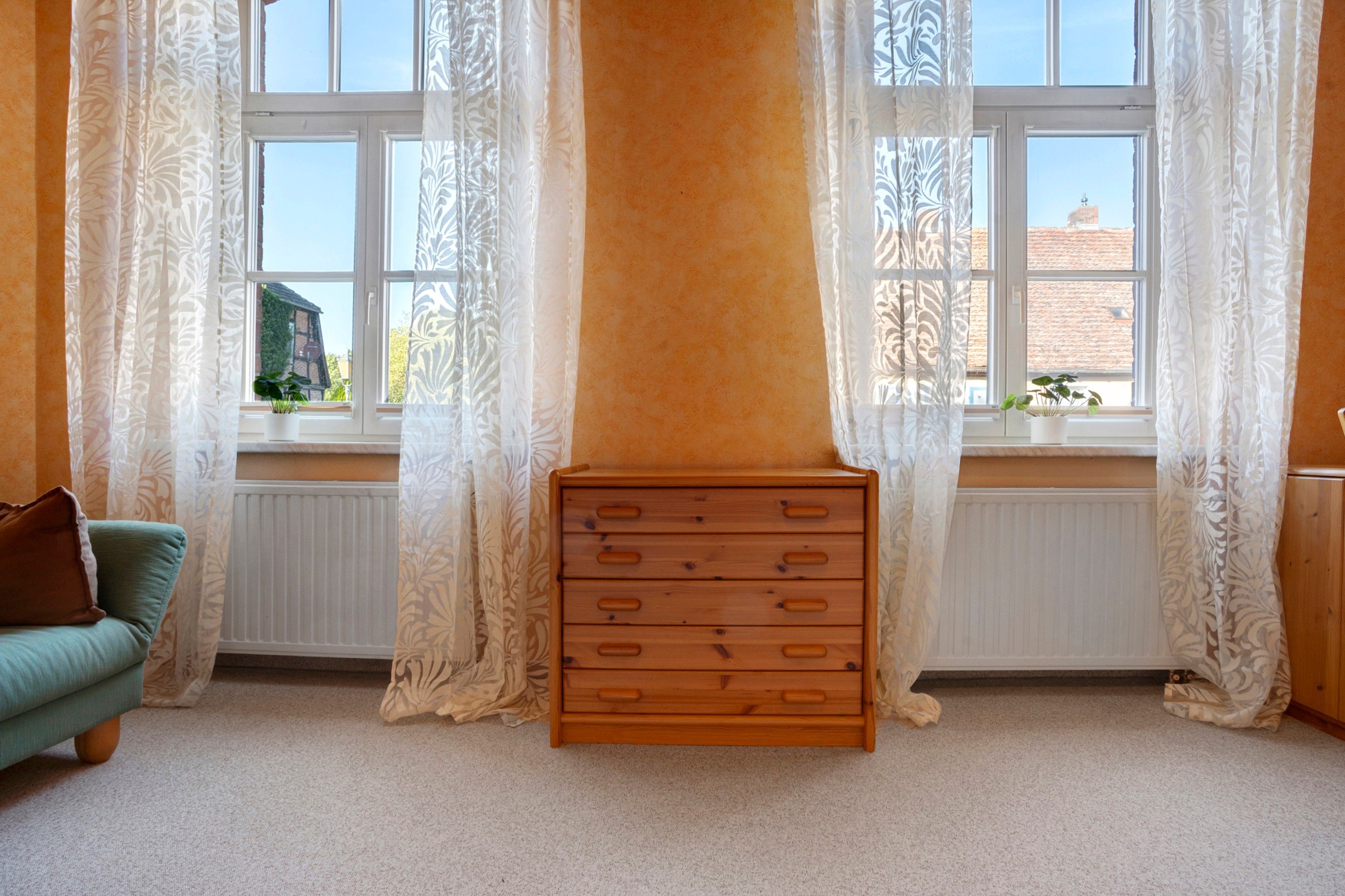 Ein Zimmer mit einem Holzkoffer, einem grünen Sofa und einem Fenster mit weißen Vorhängen.