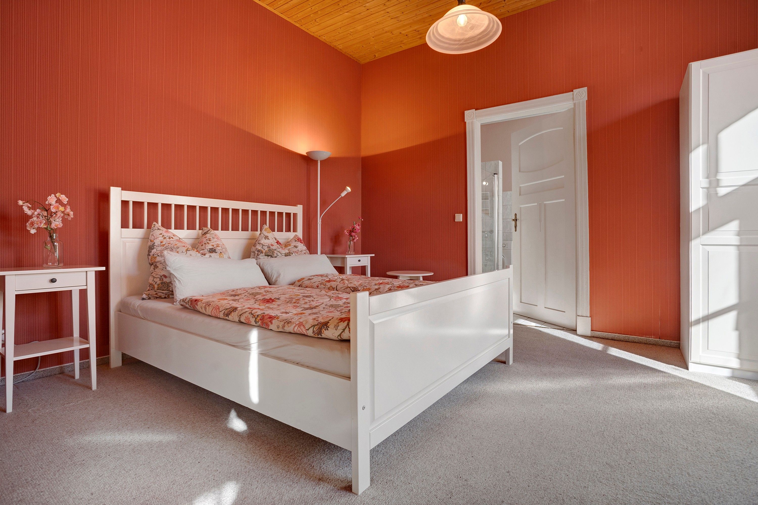 A bedroom with a white bed, a nightstand, a bedside table, a floor lamp, and a door.