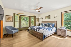 A bedroom with a bed, a chair, a nightstand, a ceiling fan, and large windows.