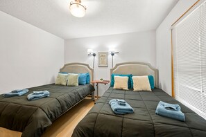 Quarto de hotel com duas camas, cada uma com cabeceira, mesa de cabeceira e luminária.