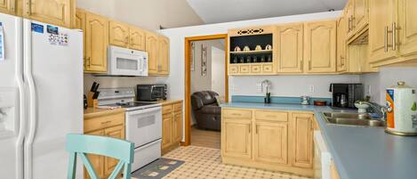 A compact kitchen with wooden cabinets, a microwave, an oven, a sink, and a chair.