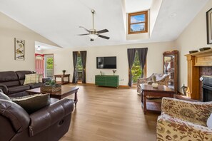 A spacious living room with a ceiling fan, a fireplace, a television, and a large window with curtains.