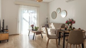 Un salon moderne comprenant un canapé, une table à manger, des chaises, un téléviseur et une fenêtre avec des rideaux.