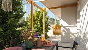 Un espace de restauration en plein air avec une table dressée pour deux personnes, entouré de verdure et d’une pergola en bois.