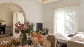 Une pièce bien éclairée, avec une table à manger dressée pour deux personnes, un lit avec vue, une télévision et une porte donnant sur une autre pièce.